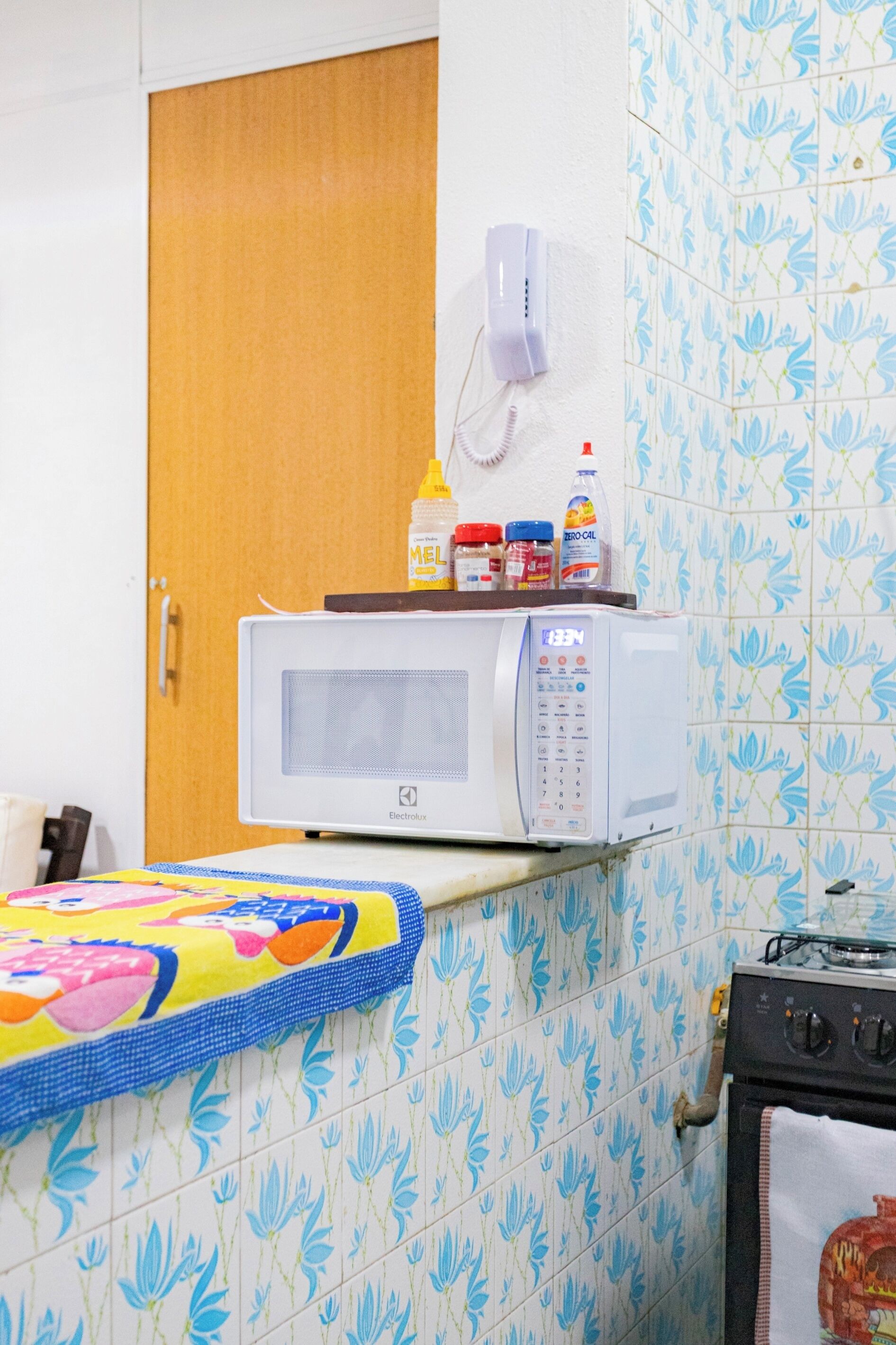 A kitchen with a microwave on a countertop, a stove, and a wall-mounted telephone.
