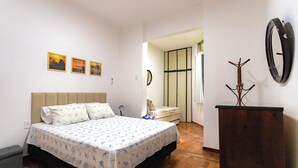 Een slaapkamer met een bed, een kapstok, een spiegel en een deur naar een andere kamer.