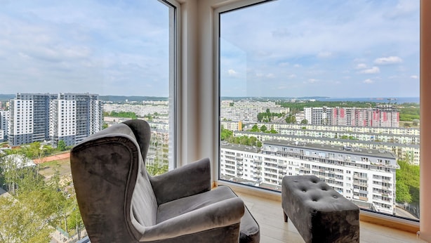 Un salon moderne avec une grande fenêtre, un fauteuil gris et un petit pouf.