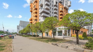 Un chemin pavé bordé d’arbres et un immeuble à plusieurs étages doté de balcons.