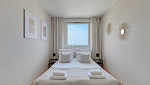 Un lit double bien fait, avec du linge de lit blanc, deux tables de chevet avec des lampes et une grande fenêtre avec des rideaux.