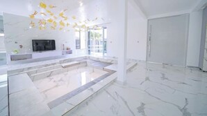 Un interior espacioso y moderno con suelo de mármol, una zona central amplia y un televisor sobre un mueble blanco.