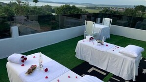 Terraza en la azotea con dos mesas de masaje, cada una con mantel blanco y almohadas, sobre césped artificial.