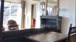 Een kamer met hoge plafonds, een open haard, een eettafel met versierde stoelen, een grote spiegel en een opgeplakt hert.