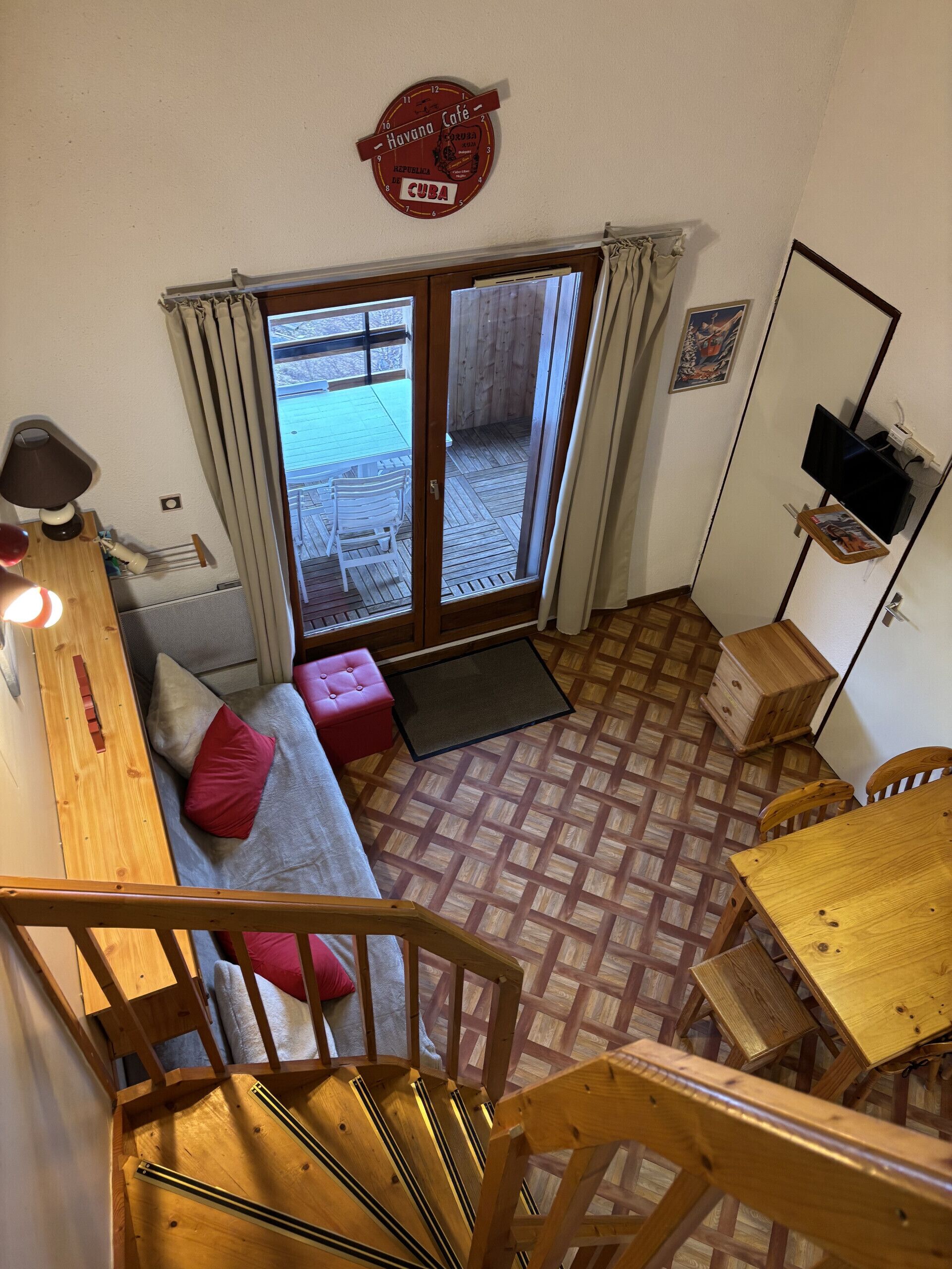 A cozy room with a wooden staircase, a sofa with cushions, a small table, and a TV mounted on the wall.