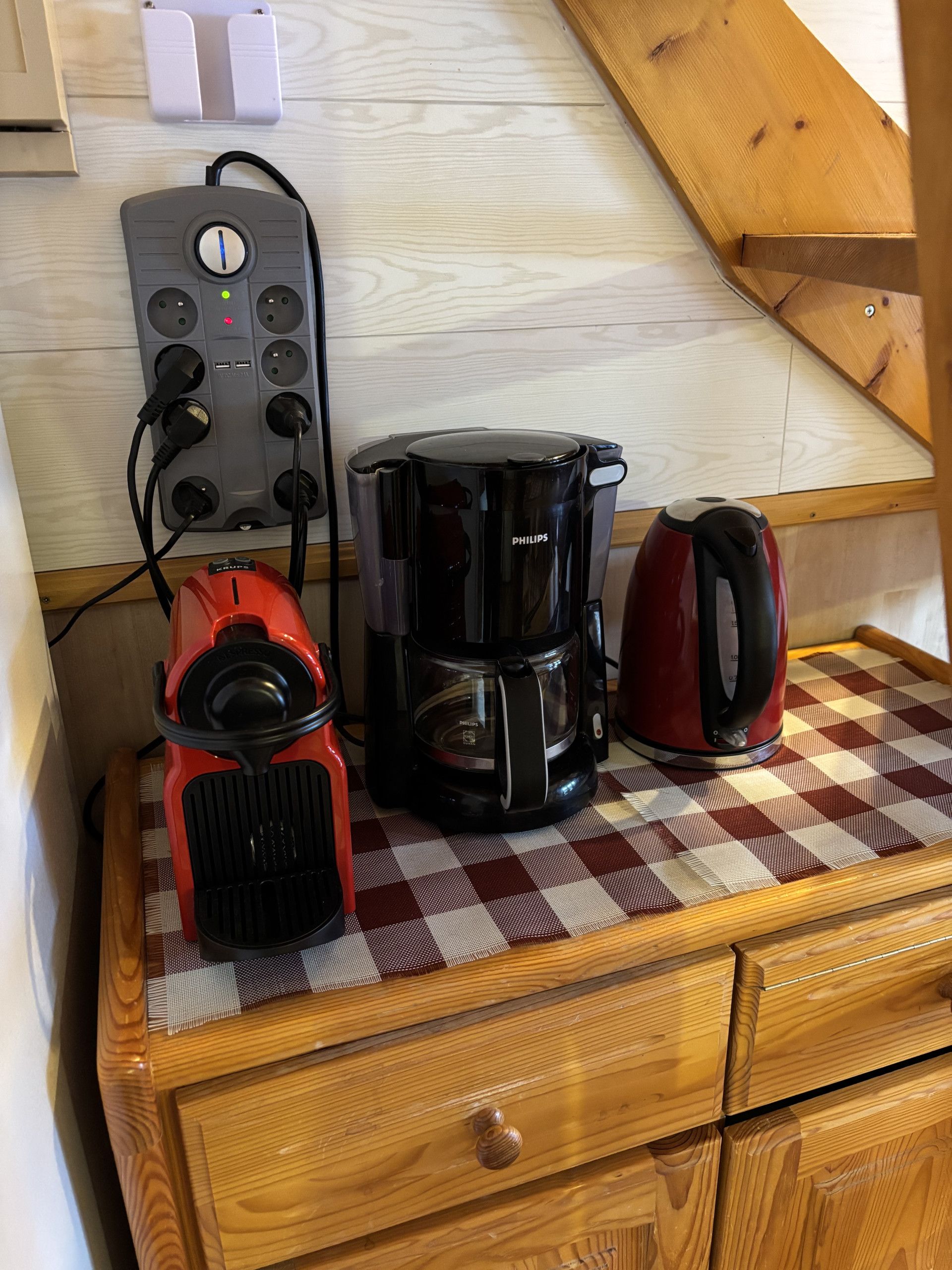 A kitchenette with a coffee maker, a red electric kettle, and a power strip on a wooden countertop.