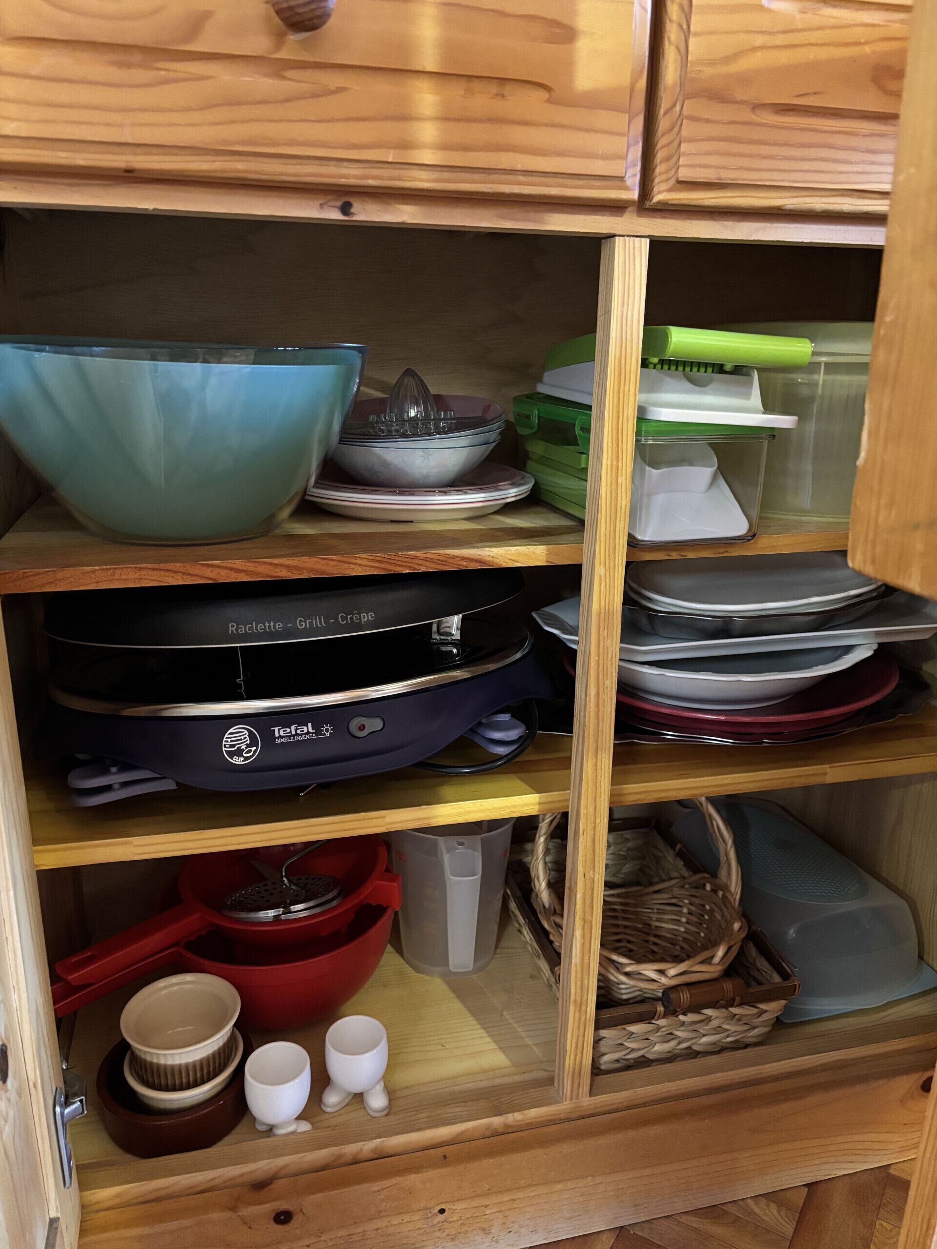 A kitchen cabinet with various kitchenware, including bowls, plates, and a food processor.