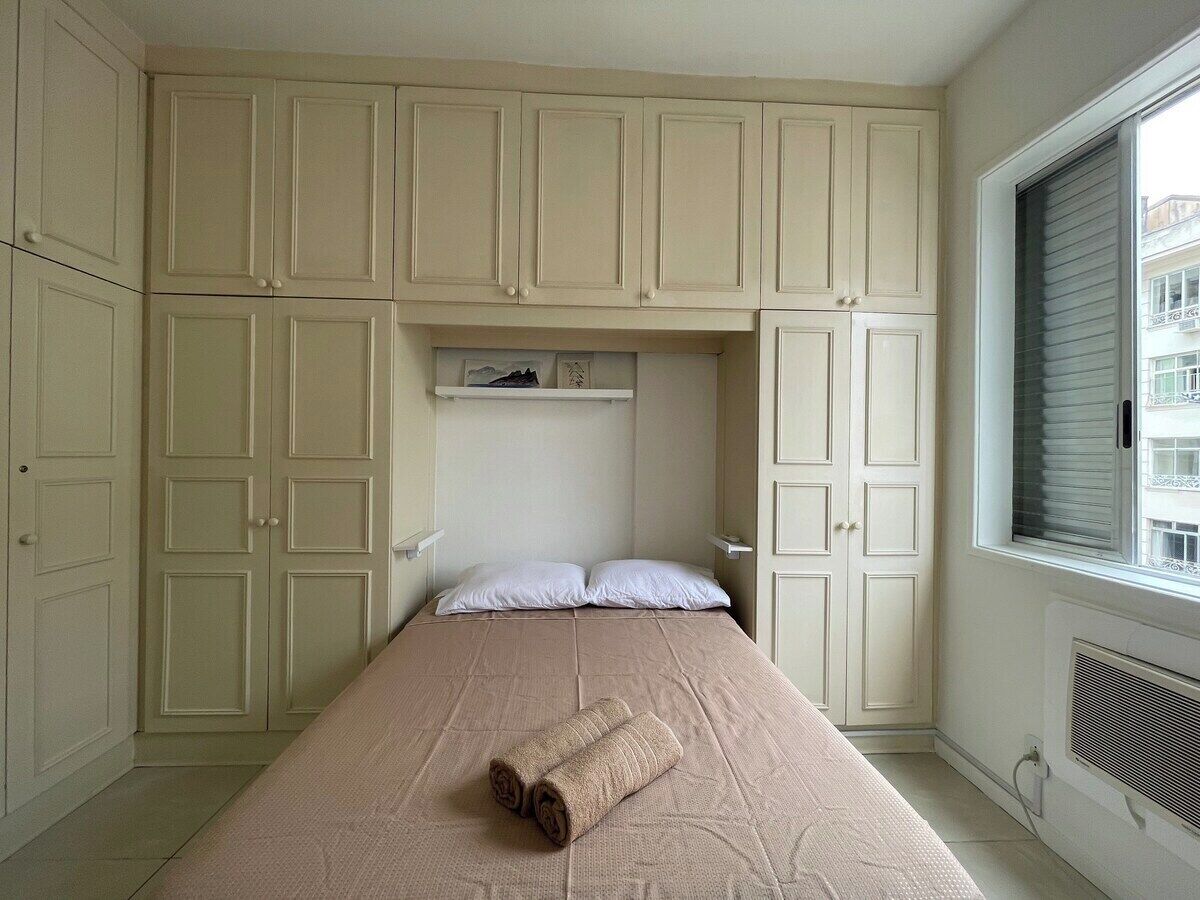 A bedroom with a single bed, beige walls, and a window with blinds.