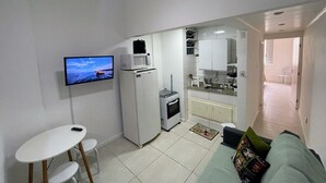 Un espacio habitable compacto con kitchenette, una zona de comedor con una mesa pequeña y sillas, y un sofá con un cojín colorido.