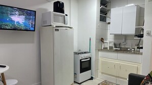 Cocina compacta con refrigerador, microondas, estufa y horno pequeño. Hay un área de comedor con una mesa y sillas, y un televisor montado en la pared.