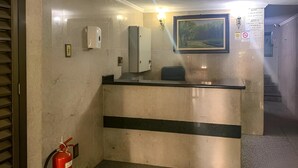 Zona de recepción con mostrador, extintor, dispensador de gel hidroalcohólico y un cuadro en la pared.