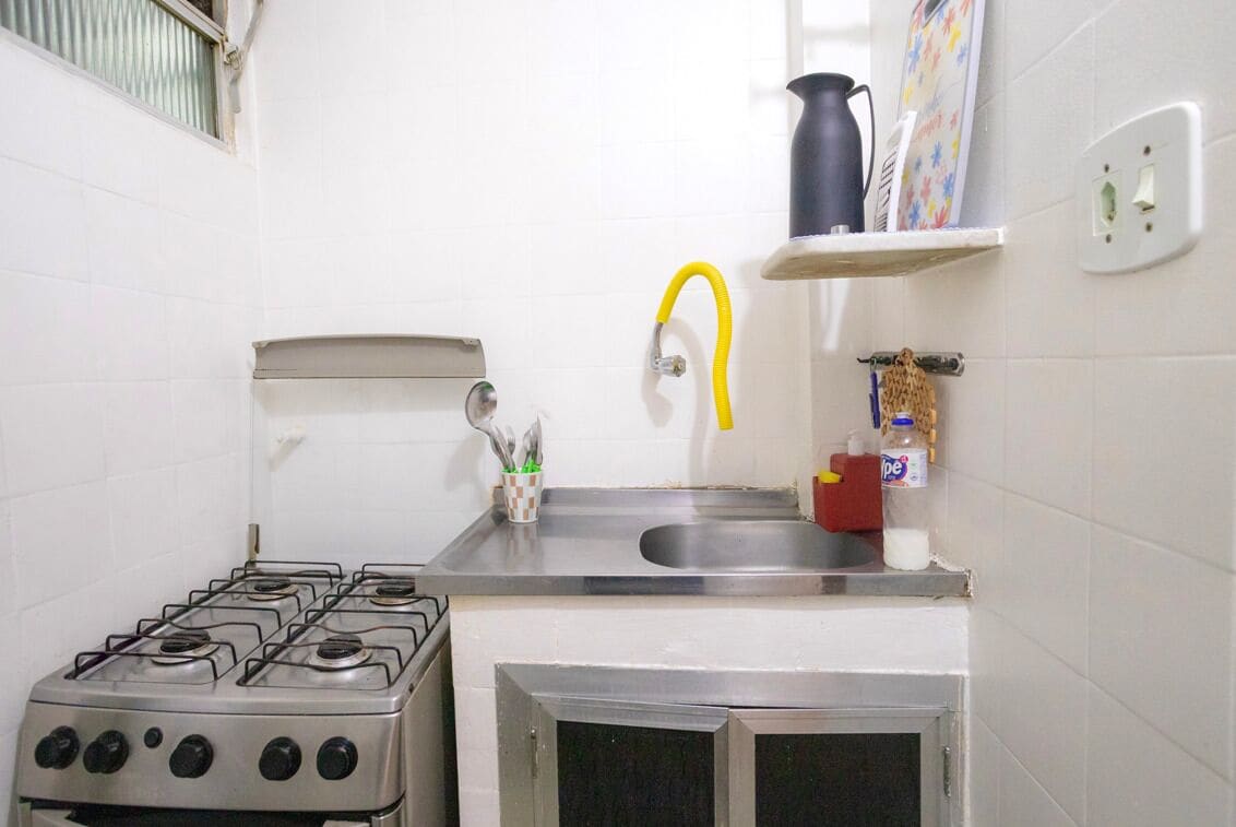 Une cuisine de taille réduite, équipée d’une cuisinière à gaz, d’un évier et d’un petit placard.