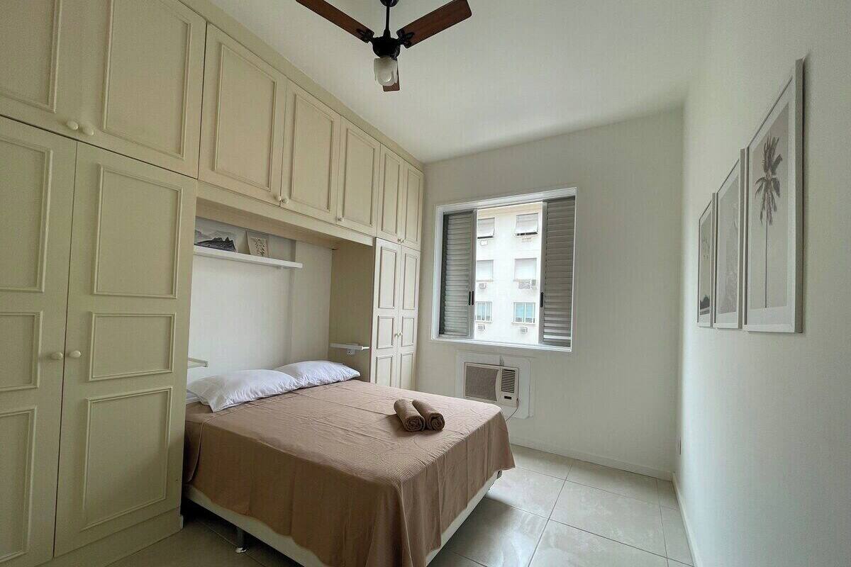 A bedroom with a bed, a ceiling fan, a window with blinds, and a wall-mounted air conditioner.