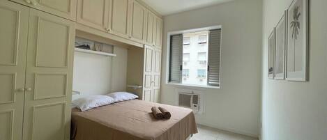 Un dormitorio con cama, ventilador de techo, ventana con persianas y aire acondicionado de pared.