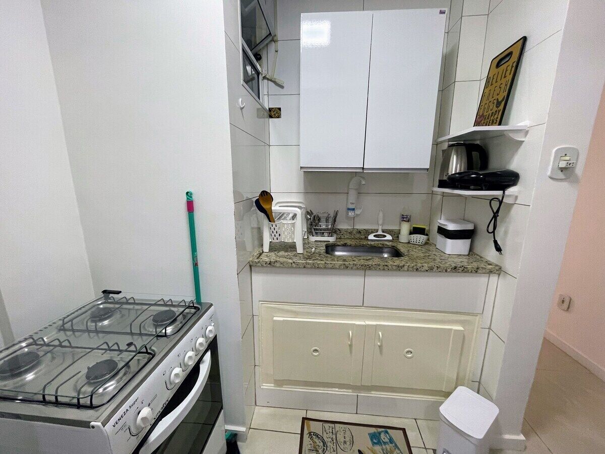 A compact kitchen with white cabinets, a gas stove, a sink, and a countertop with various kitchen items.