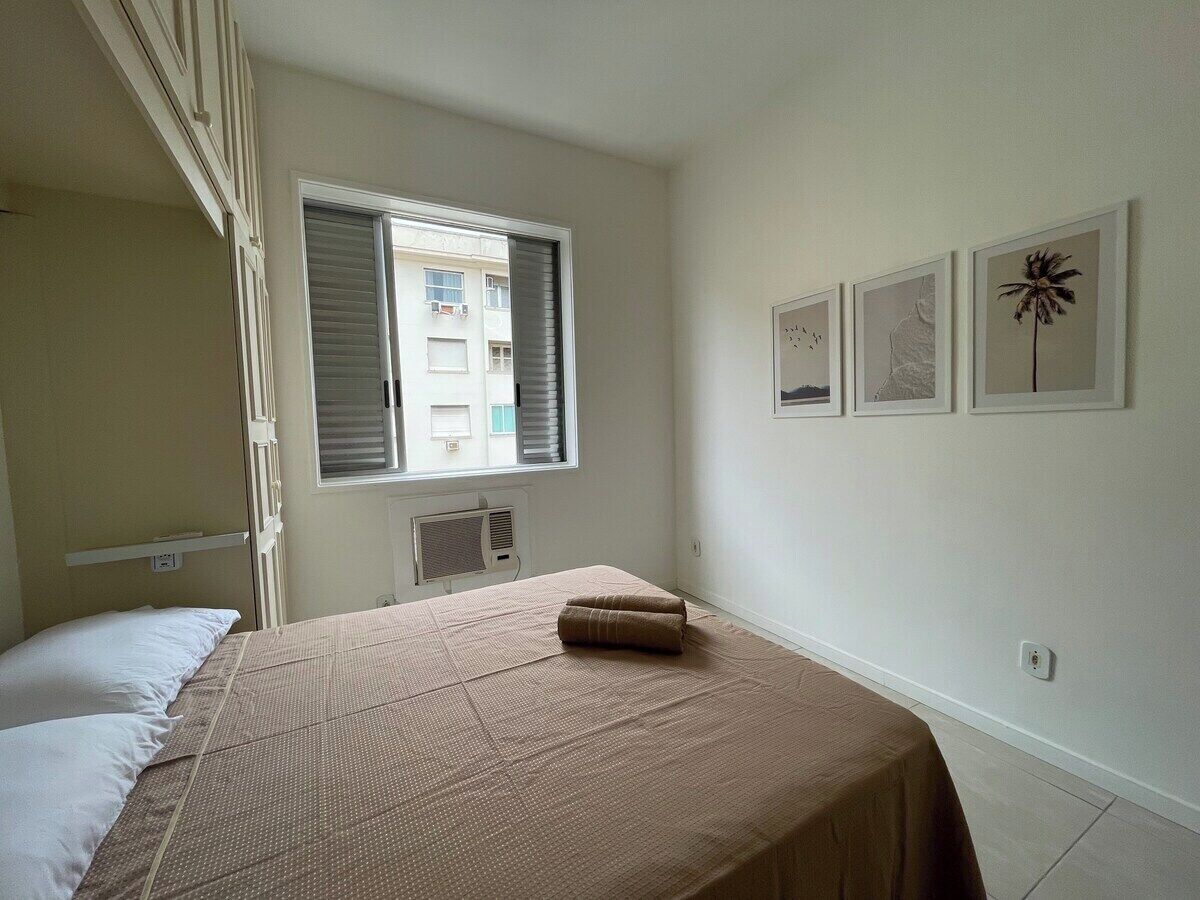 A bedroom with a bed, a window with blinds, a radiator, and three framed pictures on the wall.