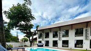 Uma área de piscina com espreguiçadeiras, piscina e um edifício com várias janelas e aparelhos de ar condicionado.