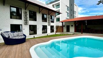 A modern building with a swimming pool, outdoor seating, and multiple air conditioning units.