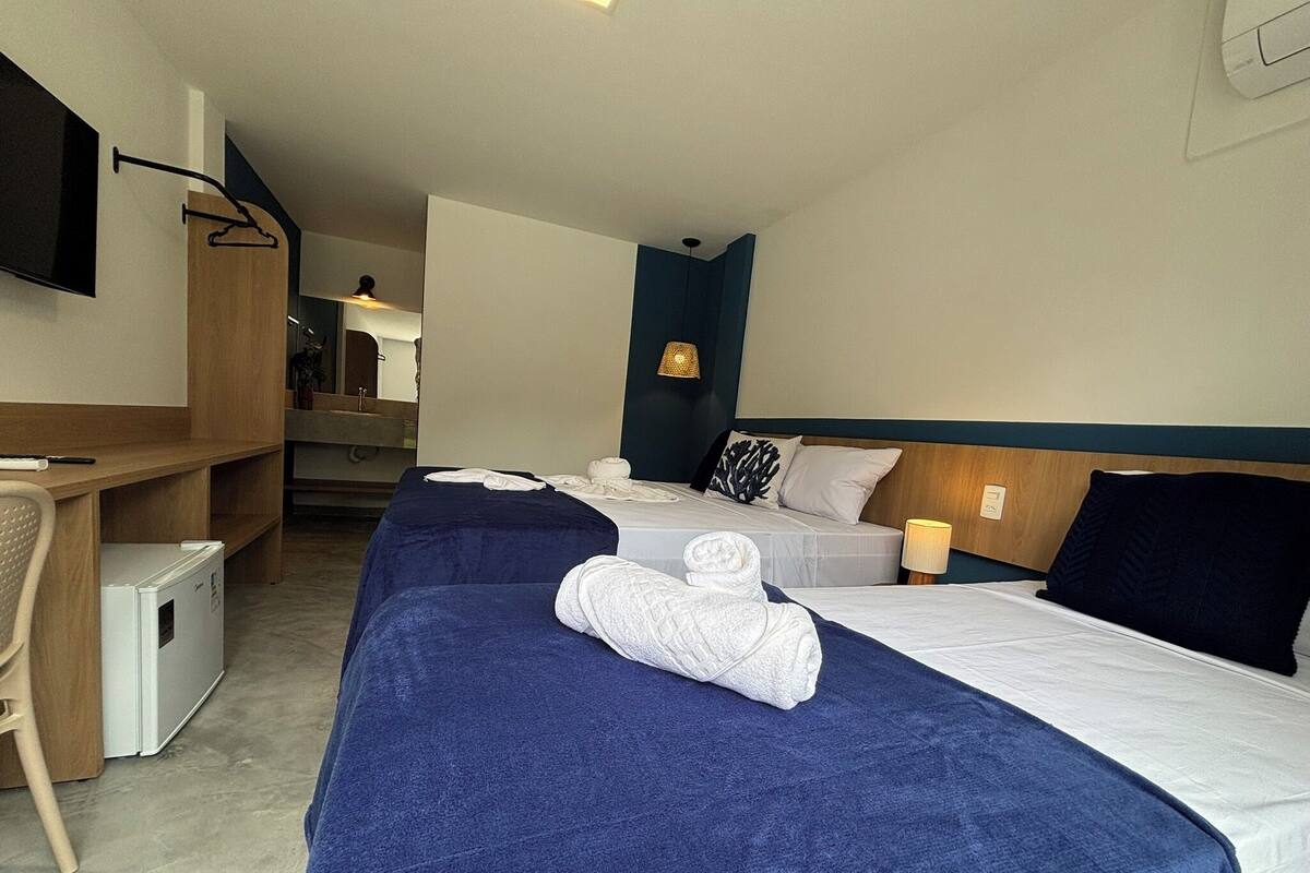 A hotel room with two beds, a desk, a chair, and a TV.