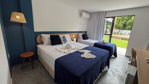 Quarto de hotel com duas camas, um banquinho, ar condicionado e vista para o exterior.
