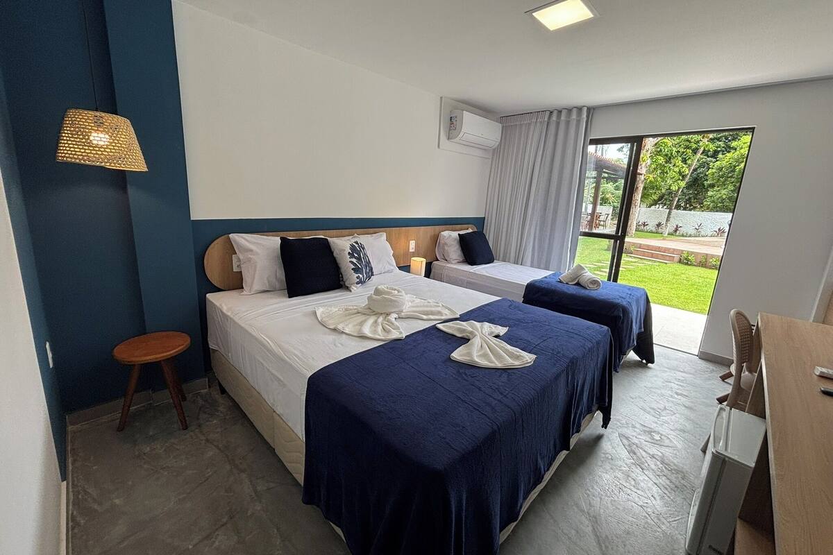 A hotel room with two beds, a small stool, an air conditioning unit, and a view of the outdoors.