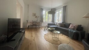 A living room with a sofa, a dining table with chairs, a TV, and a window with curtains. - Rudbecksgatan  (Eskilstuna)