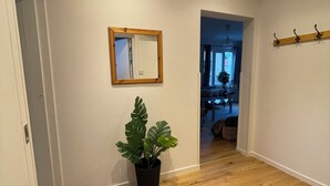 A hallway with wooden flooring, a potted plant, a striped rug, a mirror, and a coat rack. - Rudbecksgatan  (Eskilstuna)