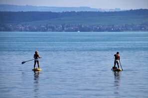 Two people paddleboarding on a calm lake with a town in the background.