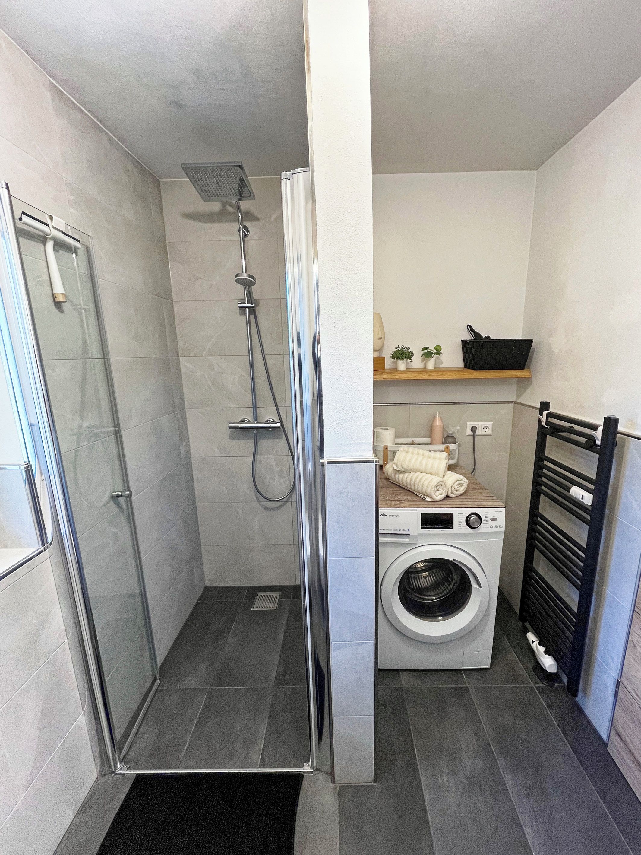 Ein kleines Badezimmer mit Dusche, Waschmaschine und Wäscheständer.