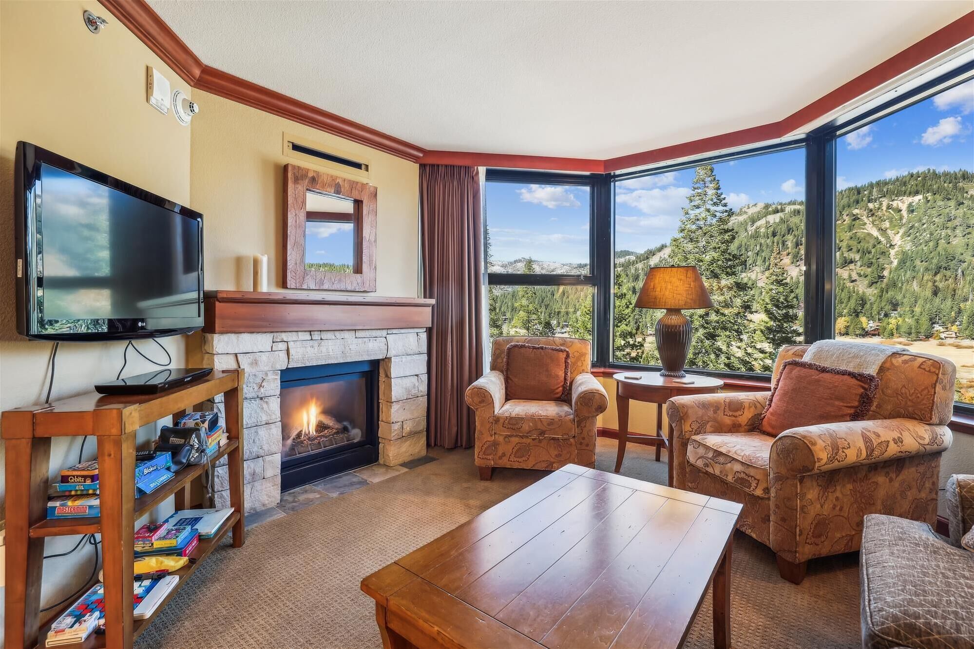 A cozy living room with a fireplace, a television, and a view of a mountainous landscape.
