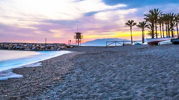 Una spiaggia con una torretta per i bagnini, palme e barche.