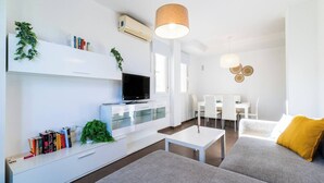 Un soggiorno moderno con un divano, un tavolino, una TV su un mobile bianco e un'area pranzo con sedie e tavolo.
