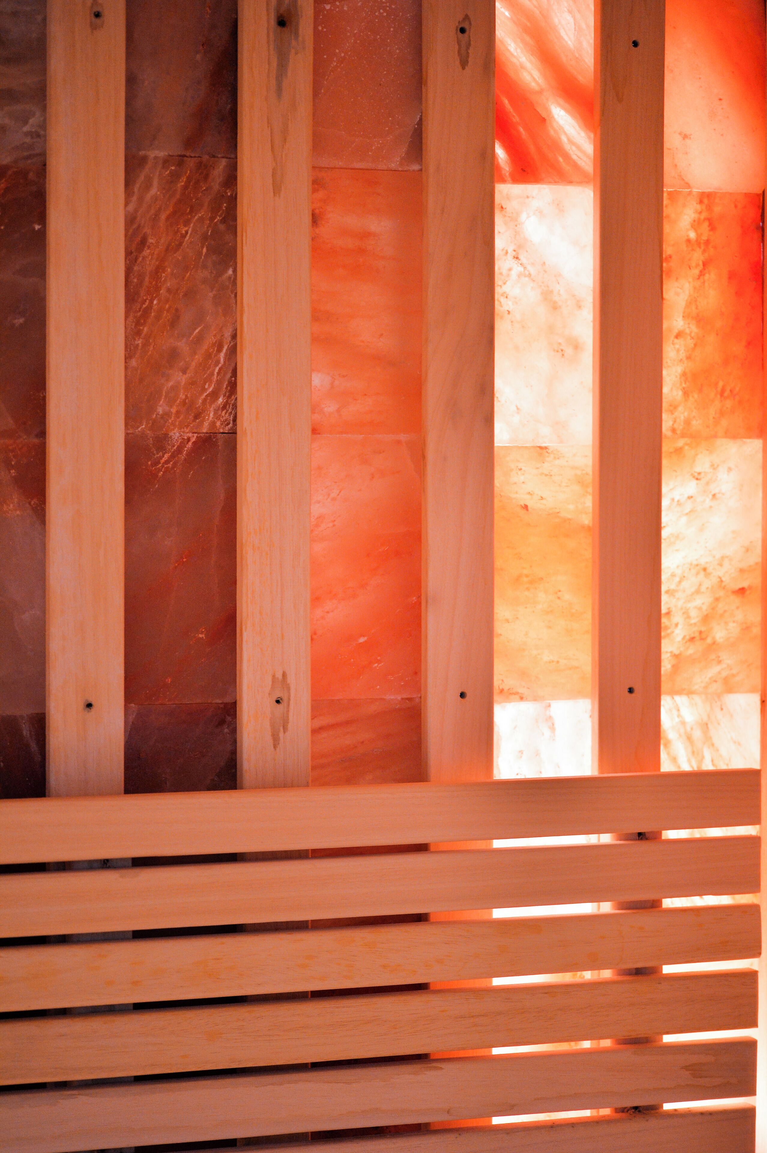 A wooden bench with a slatted design, positioned against a wall with a textured surface.