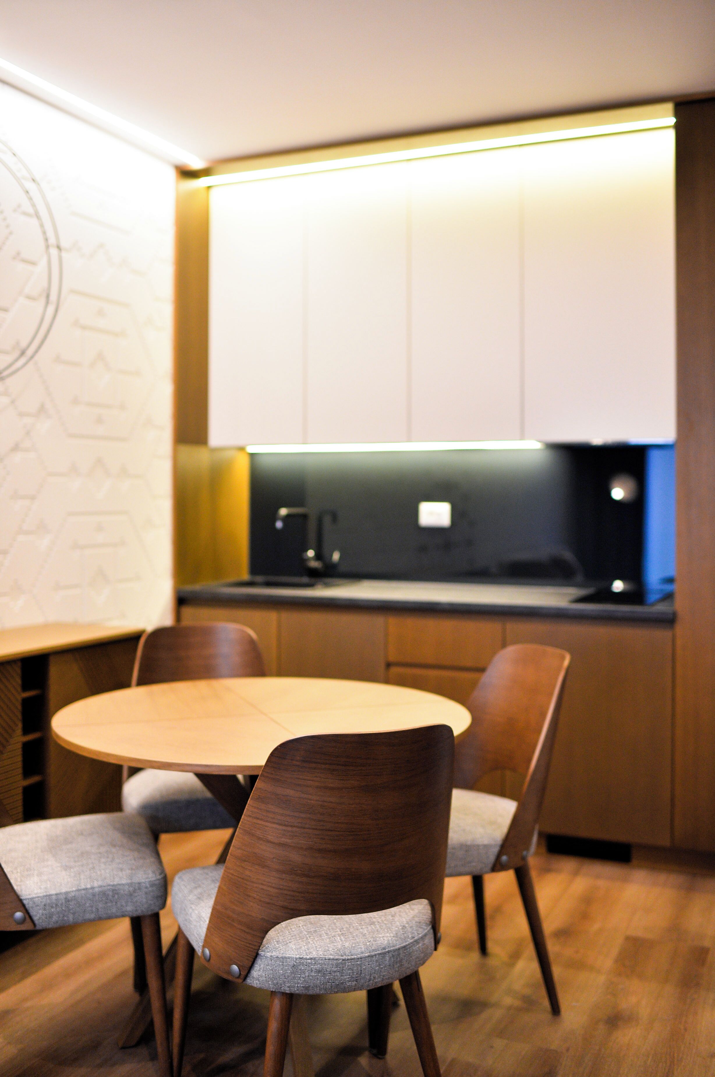A modern kitchen with wooden cabinets, a round dining table, and grey upholstered chairs.