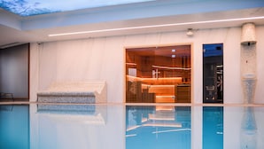 Una piscina interior moderna con agua cristalina, un banco de madera y una zona de recepción con puerta de cristal.