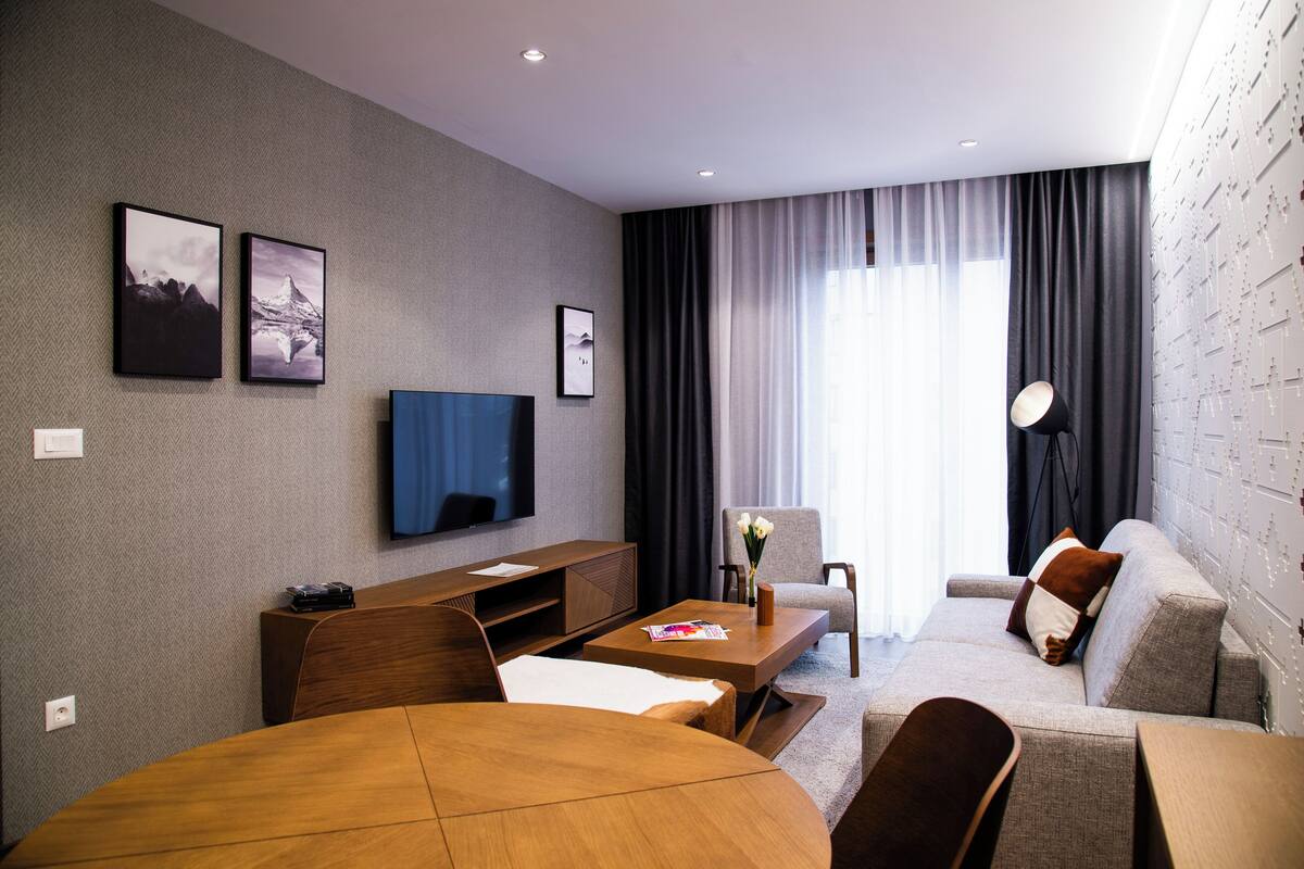 Una habitación de hotel moderna con una televisión de pantalla plana, un sofá, una mesa de comedor y una mesita de centro.