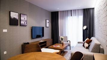 Una habitación de hotel moderna con una televisión de pantalla plana, un sofá, una mesa de comedor y una mesita de centro.