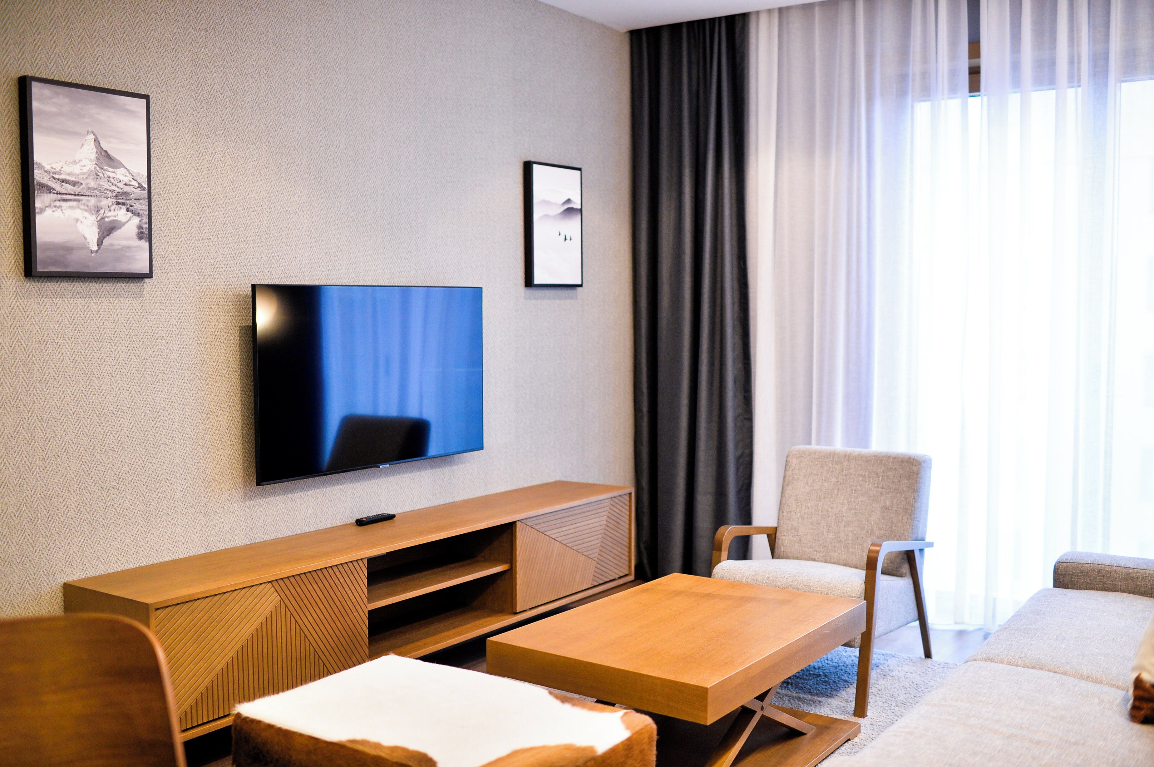 A modern hotel room with a flat-screen TV mounted on the wall, a wooden console table, a sofa, and a small coffee table.