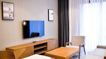 A modern hotel room with a flat-screen TV mounted on the wall, a wooden console table, a sofa, and a small coffee table.