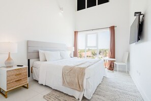 A bedroom with a bed, bedside table, lamp, and a view of the outdoors through a window. - Spacious Condo with Pool Access in Noord (Noord)