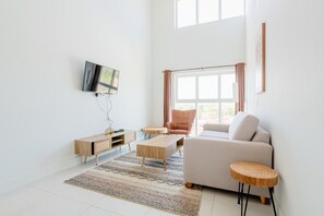 Ein modernes Wohnzimmer mit einer Couch, einem Couchtisch, einem Fernseher und einem großen Fenster mit Vorhängen.