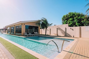 Une piscine dotée d’une terrasse ensoleillée, de chaises longues et d’un espace couvert avec des portes vitrées.
