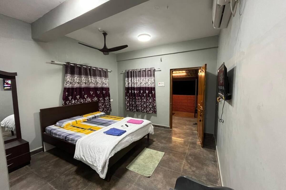 A bedroom with a bed, a ceiling fan, a TV, and a door leading to another room.