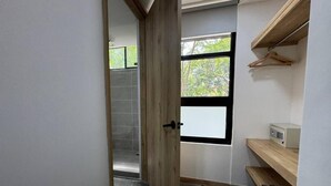 A narrow hallway with a wooden door leading to a bathroom with a shower and a window with a view of greenery. - Akela Park (Medellín)