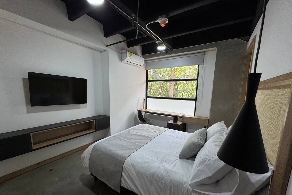 A modern bedroom with a bed, a mounted TV, a window, and a hanging lamp.