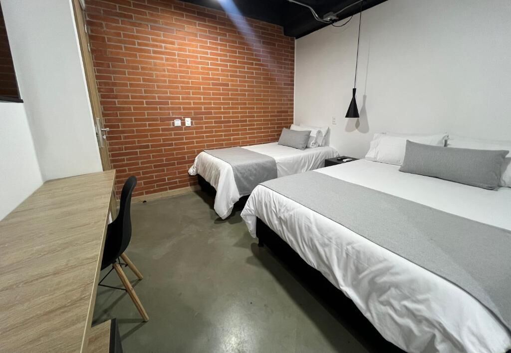 A room with two beds, a desk, and a brick wall.