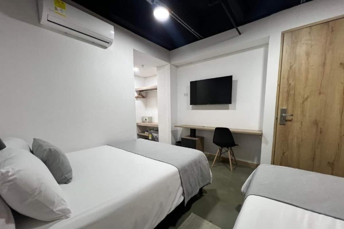A hotel room with two beds, a desk, a TV, and a wooden door.