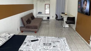 Una habitación de hotel pequeña con sofá, una mesita, televisión y un periódico extendido en el suelo.