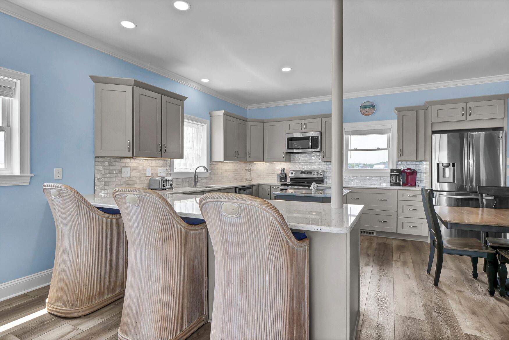 A modern kitchen with grey cabinets, a large island with bar stools, stainless steel appliances, and a blue accent wall.