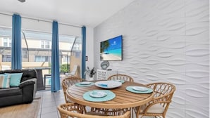 Een eetgedeelte met een ronde houten tafel, rieten stoelen en uitzicht op zee door grote ramen.